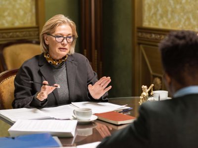 Confident blond female lawyer talking to young African male colleague sitting in front of her