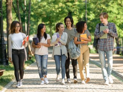 Picture of multiethnic group of young cheerful students walking while talking. Looking aside.