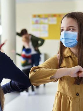Girls greeting at school with their elbows during the COVID-19 pandemic