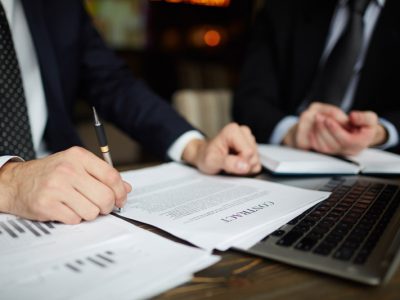 Closeup portrait of unrecognizable successful businessman wearing black formal suit reviewing documents and signing contract during meeting