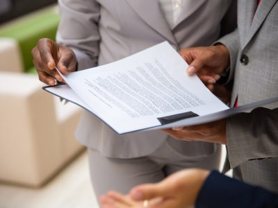 Diverse business partners reading contract together. Business man and woman wearing formal suits, standing and holding open folder with document. Agreement concept