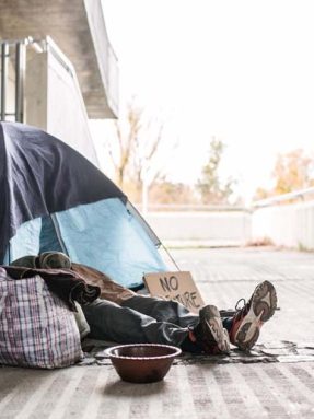 Legs and feet of homeless beggar man lying on the ground outdoors in city, sleeping in tent and asking for money donation.