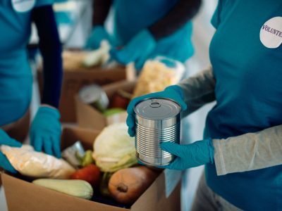 Unrecognizable people packing food in donation boxes while working as volunteers in charitable foundation.
